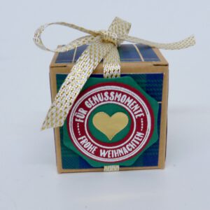 Genussmomente, handdekorierte geschenkschachtel mit stern und schriftzug, geschenkbox mit weihnachtlichem band und etikett, detailaufnahme stern auf geschenkschachtel, geschenkschachtel von oben mit schleife, seitenansicht handdekorierte weihnachtsschachtel, geschenkschachtel mit karomuster und band, weihnachtliche geschenkverpackung mit lecker-lecker motiv