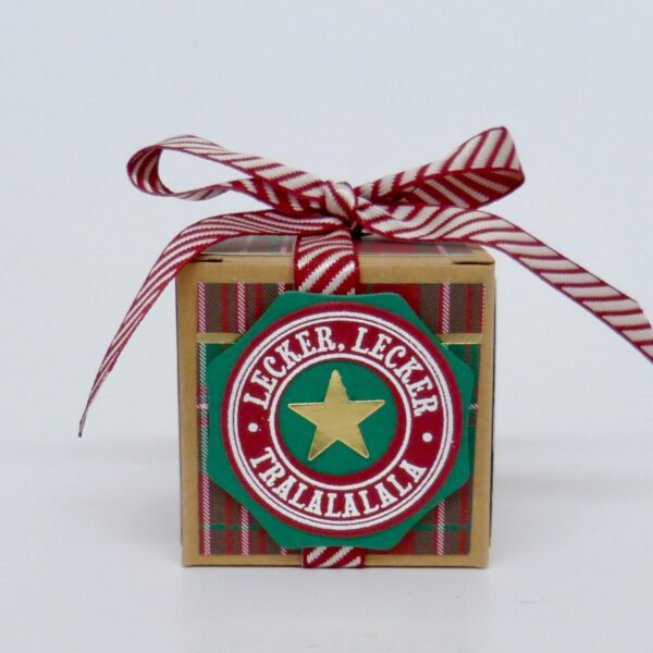 handdekorierte geschenkschachtel mit stern und schriftzug, geschenkbox mit weihnachtlichem band und etikett, detailaufnahme stern auf geschenkschachtel, geschenkschachtel von oben mit schleife, seitenansicht handdekorierte weihnachtsschachtel, geschenkschachtel mit karomuster und band, weihnachtliche geschenkverpackung mit lecker-lecker motiv