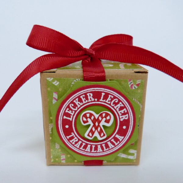 handdekorierte geschenkschachtel mit stern und schriftzug, geschenkbox mit weihnachtlichem band und etikett, detailaufnahme stern auf geschenkschachtel, geschenkschachtel von oben mit schleife, seitenansicht handdekorierte weihnachtsschachtel, geschenkschachtel mit karomuster und band, weihnachtliche geschenkverpackung mit lecker-lecker motiv