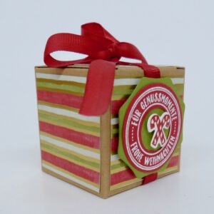 handdekorierte geschenkschachtel mit stern und schriftzug, geschenkbox mit weihnachtlichem band und etikett, detailaufnahme stern auf geschenkschachtel, geschenkschachtel von oben mit schleife, seitenansicht handdekorierte weihnachtsschachtel, geschenkschachtel mit karomuster und band, weihnachtliche geschenkverpackung mit lecker-lecker motiv