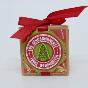 Genussmomente Tannenbaum, handdekorierte geschenkschachtel mit stern und schriftzug, geschenkbox mit weihnachtlichem band und etikett, detailaufnahme stern auf geschenkschachtel, geschenkschachtel von oben mit schleife, seitenansicht handdekorierte weihnachtsschachtel, geschenkschachtel mit karomuster und band, weihnachtliche geschenkverpackung mit lecker-lecker motiv