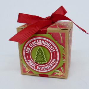 Genussmomente Tannenbaum, handdekorierte geschenkschachtel mit stern und schriftzug, geschenkbox mit weihnachtlichem band und etikett, detailaufnahme stern auf geschenkschachtel, geschenkschachtel von oben mit schleife, seitenansicht handdekorierte weihnachtsschachtel, geschenkschachtel mit karomuster und band, weihnachtliche geschenkverpackung mit lecker-lecker motiv