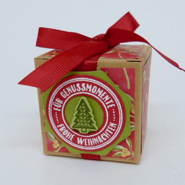 Genussmomente Tannenbaum, handdekorierte geschenkschachtel mit stern und schriftzug, geschenkbox mit weihnachtlichem band und etikett, detailaufnahme stern auf geschenkschachtel, geschenkschachtel von oben mit schleife, seitenansicht handdekorierte weihnachtsschachtel, geschenkschachtel mit karomuster und band, weihnachtliche geschenkverpackung mit lecker-lecker motiv