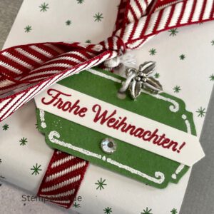 Geschenkdose Frohe Weihnachten mit Schneeflocken, Geschenkdose mit Schleifenband und Anhänger, Detailansicht Schneeflocken-Metallaccessoire, offene Geschenkdose mit Inhalt, Nahaufnahme Banderole Geschenkdose, Geschenkdose als Geschenkverpackung, handgemachte Weihnachtsdose mit Etikett