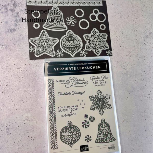 Bastelmaterialien für weihnachtliche Karten oder Projekte. Zu sehen sind grünes und rotes Tonpapier, gemustertes Designerpapier, ein Stempelset namens „Verzierte Lebkuchen“ mit passenden deutschen Sprüchen, metallische Stanzformen für Weihnachtsmotive (Stern, Glocke, Schneeflocke, Kugel), rote und weiße Kordel, goldene Zierdeckchen sowie Briefumschläge