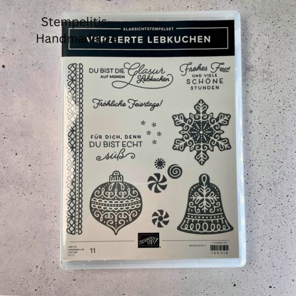 Bastelmaterialien für weihnachtliche Karten oder Projekte. Zu sehen sind grünes und rotes Tonpapier, gemustertes Designerpapier, ein Stempelset namens „Verzierte Lebkuchen“ mit passenden deutschen Sprüchen, metallische Stanzformen für Weihnachtsmotive (Stern, Glocke, Schneeflocke, Kugel), rote und weiße Kordel, goldene Zierdeckchen sowie Briefumschläge