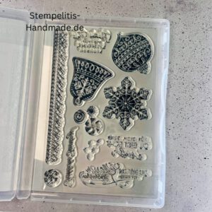 Bastelmaterialien für weihnachtliche Karten oder Projekte. Zu sehen sind grünes und rotes Tonpapier, gemustertes Designerpapier, ein Stempelset namens „Verzierte Lebkuchen“ mit passenden deutschen Sprüchen, metallische Stanzformen für Weihnachtsmotive (Stern, Glocke, Schneeflocke, Kugel), rote und weiße Kordel, goldene Zierdeckchen sowie Briefumschläge