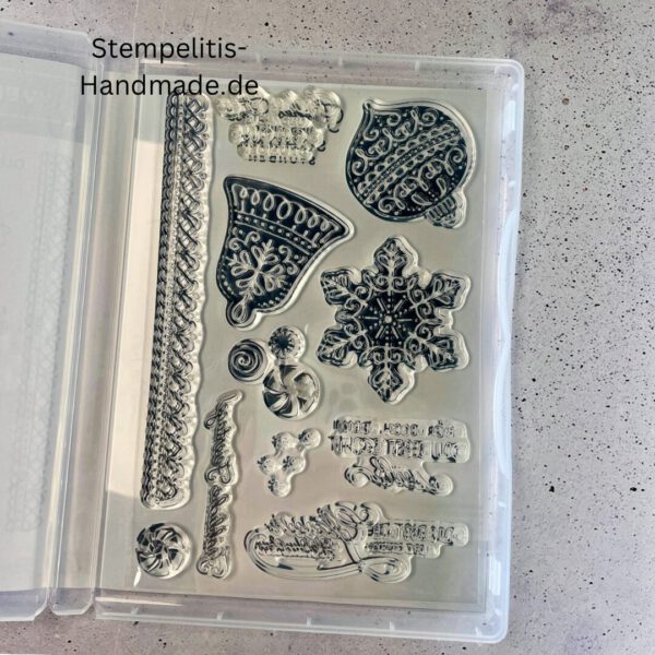 Bastelmaterialien für weihnachtliche Karten oder Projekte. Zu sehen sind grünes und rotes Tonpapier, gemustertes Designerpapier, ein Stempelset namens „Verzierte Lebkuchen“ mit passenden deutschen Sprüchen, metallische Stanzformen für Weihnachtsmotive (Stern, Glocke, Schneeflocke, Kugel), rote und weiße Kordel, goldene Zierdeckchen sowie Briefumschläge