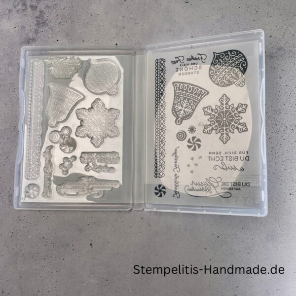 Bastelmaterialien für weihnachtliche Karten oder Projekte. Zu sehen sind grünes und rotes Tonpapier, gemustertes Designerpapier, ein Stempelset namens „Verzierte Lebkuchen“ mit passenden deutschen Sprüchen, metallische Stanzformen für Weihnachtsmotive (Stern, Glocke, Schneeflocke, Kugel), rote und weiße Kordel, goldene Zierdeckchen sowie Briefumschläge