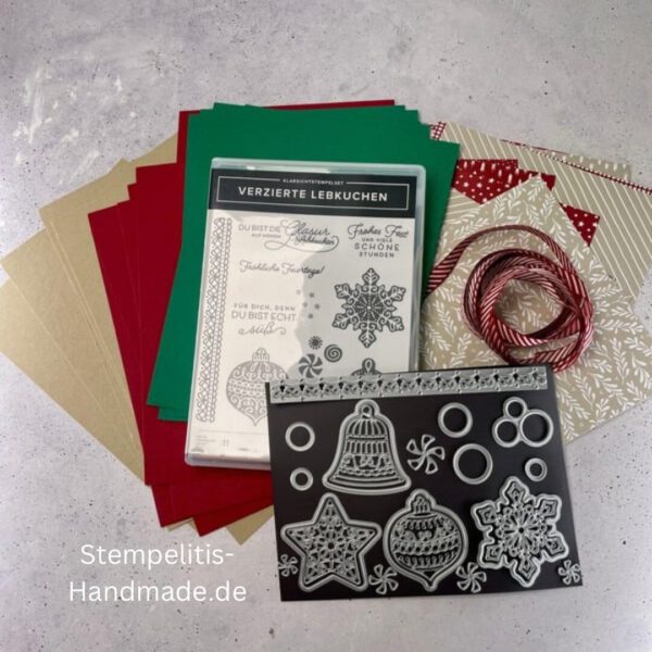 Bastelmaterialien für weihnachtliche Karten oder Projekte. Zu sehen sind grünes und rotes Tonpapier, gemustertes Designerpapier, ein Stempelset namens „Verzierte Lebkuchen“ mit passenden deutschen Sprüchen, metallische Stanzformen für Weihnachtsmotive (Stern, Glocke, Schneeflocke, Kugel), rote und weiße Kordel, goldene Zierdeckchen sowie Briefumschläge