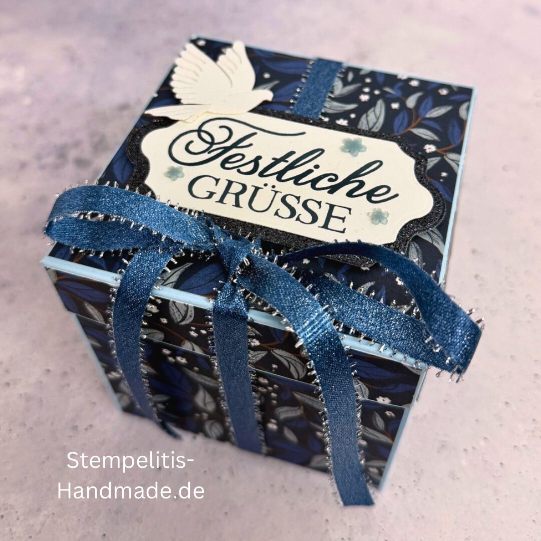 Explosionsbox in Blau mit weißer Taube, Geöffnete Explosionsbox von oben mit Geschenk und Sternenmuster, Nahaufnahme vom Deckel mit Schriftzug Festliche Grüße, Detailansicht Taube auf blauem Hintergrund, Nahaufnahme der Box innen mit Etikett, Geschenkbox im Weihnachtsdesign mit Schleife, Handgemachte Explosionsbox im festlichen Look
